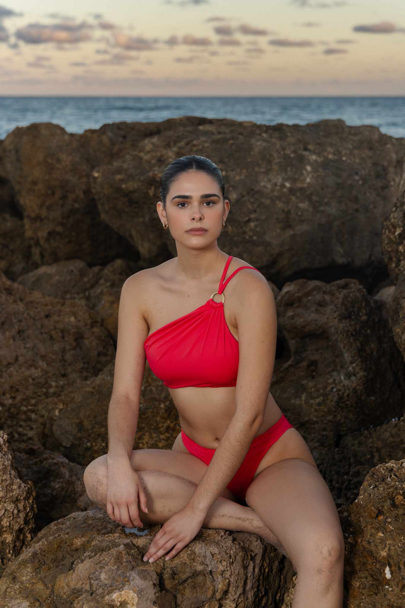 Model in red bikini sitting on beach rocks